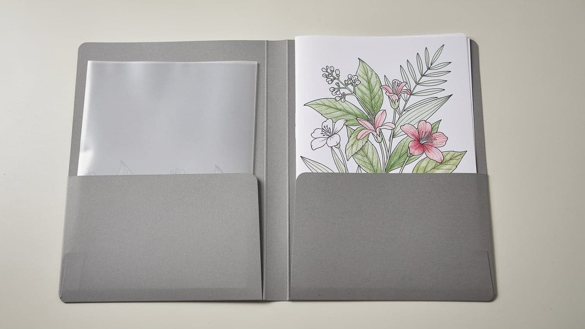 Open gray two-pocket folder holding a finished botanical coloring page and a clean protective sheet